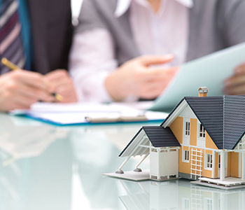 A model house on a table with real estate agents discussing in the background.