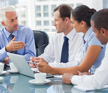 A group of four professionals in a meeting with a laptop discussing work.